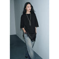 Model wearing a black oversized T-shirt with a satin hem and delicate lace trim, paired with light blue denim jeans.