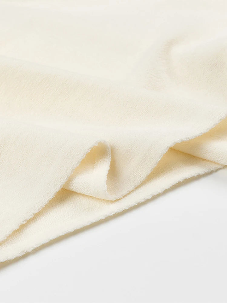 Close-up of soft cream-colored knit fabric with a plush texture and draped, irregular folds.