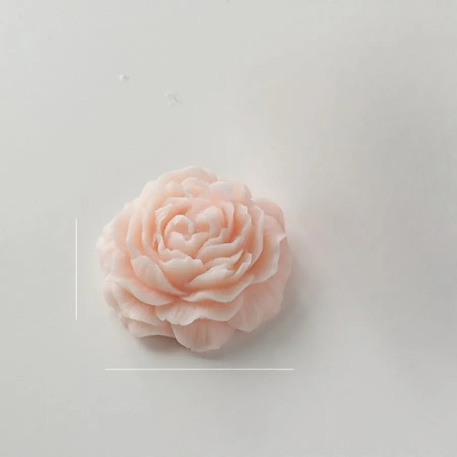 A pale pink, rose-shaped decorative wax candle with detailed, layered petals on a white background.