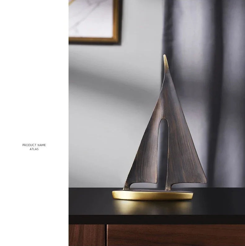 A sleek, bronze-effect resin sailboat ornament with a metallic gold base, displayed on a dark surface.