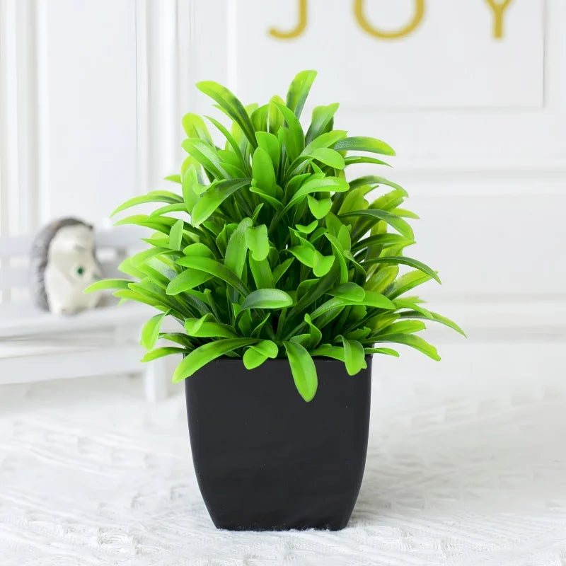 A small, bushy artificial green plant with slender leaves potted in a minimalist matte black square container.