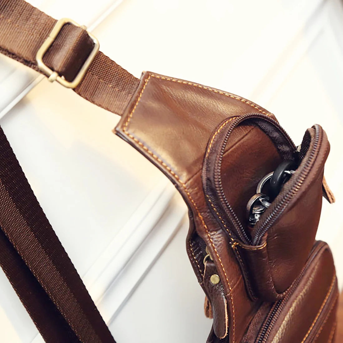 Brown leather-look crossbody sling bag with adjustable strap, zipped compartments, and contrast stitching.