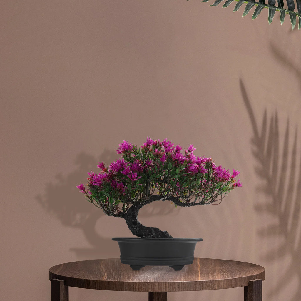 An artificial bonsai tree with vibrant magenta flowers in a black pot, displayed on a circular wooden table.