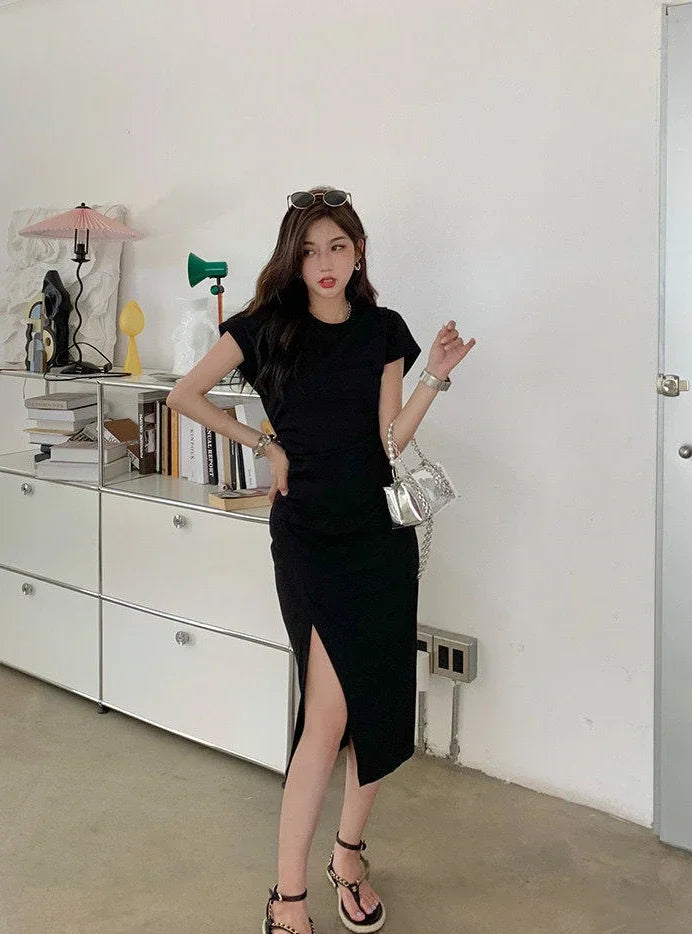 Woman wearing a black short-sleeved midi dress with a side slit, styled with a silver handbag and platform sandals.