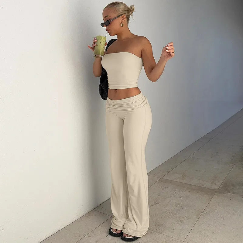 A woman wearing a cream, two-piece set featuring a strapless bandeau crop top and matching high-waisted flared trousers.