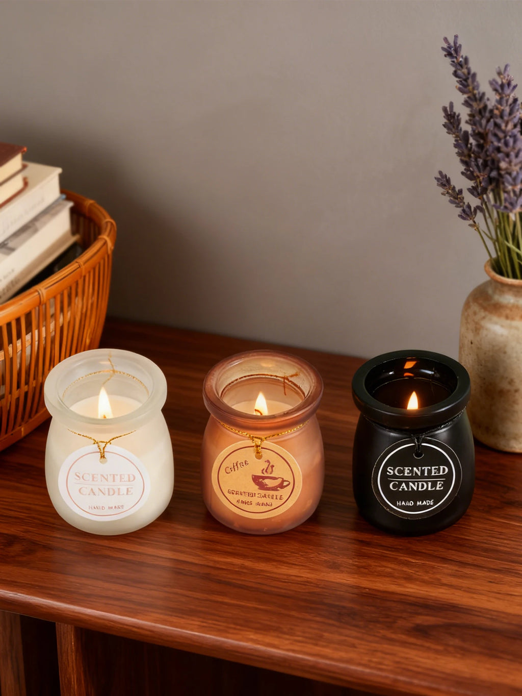 Three burning scented candles in white, brown, and black frosted glass jars with hanging circular labels on wood table.
