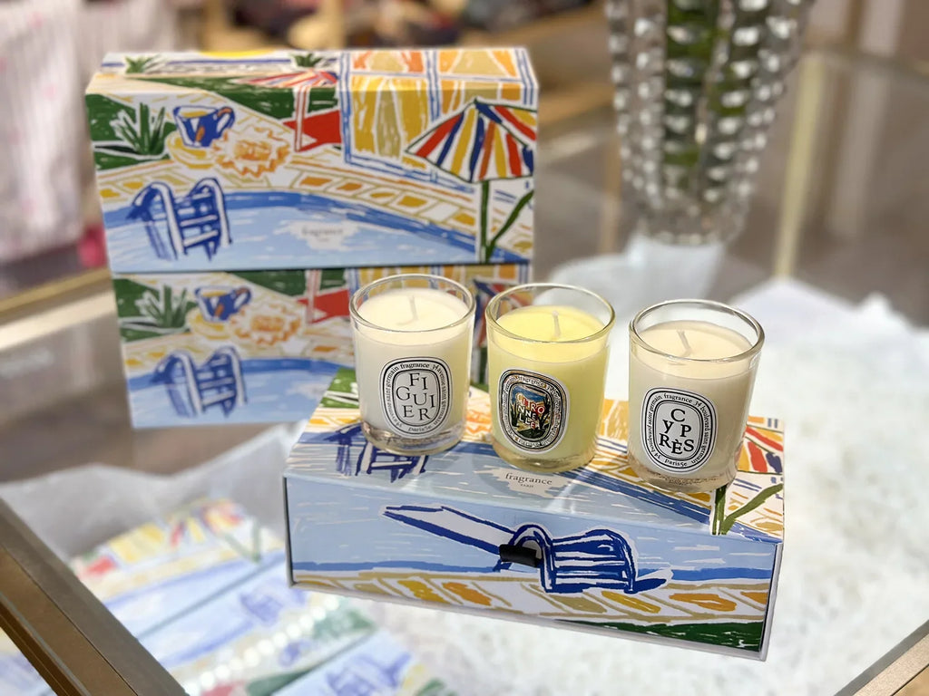 Three scented candles in glass votives presented with a colourful, illustrated gift box featuring a sunny pool scene.