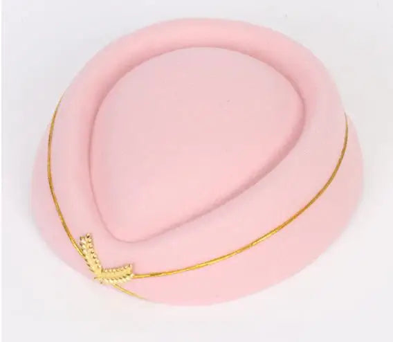 A pale pink vintage-style pillbox stewardess hat, detailed with a thin gold trim and a small gold wing emblem.
