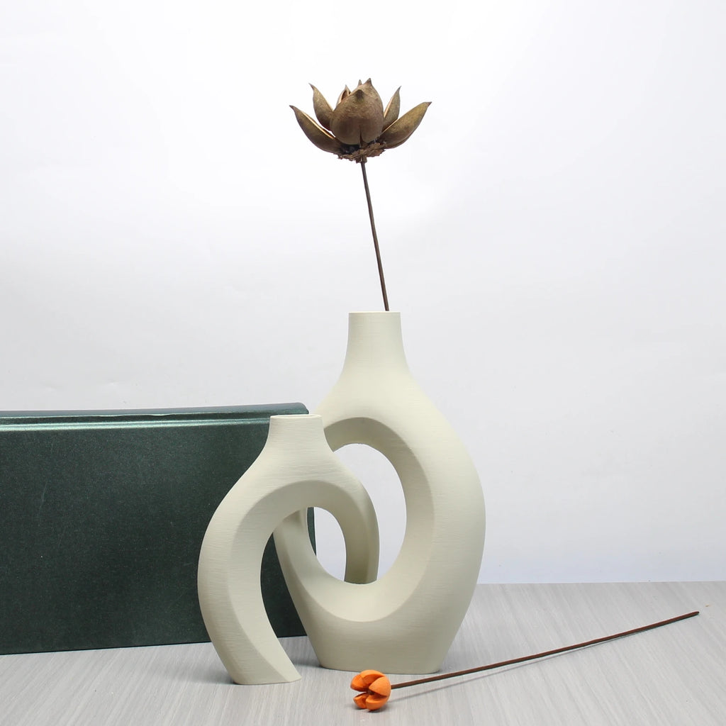 Two cream-coloured ceramic vases with a modern, sculptural Bohemian design and cut-out centres on a wooden surface.