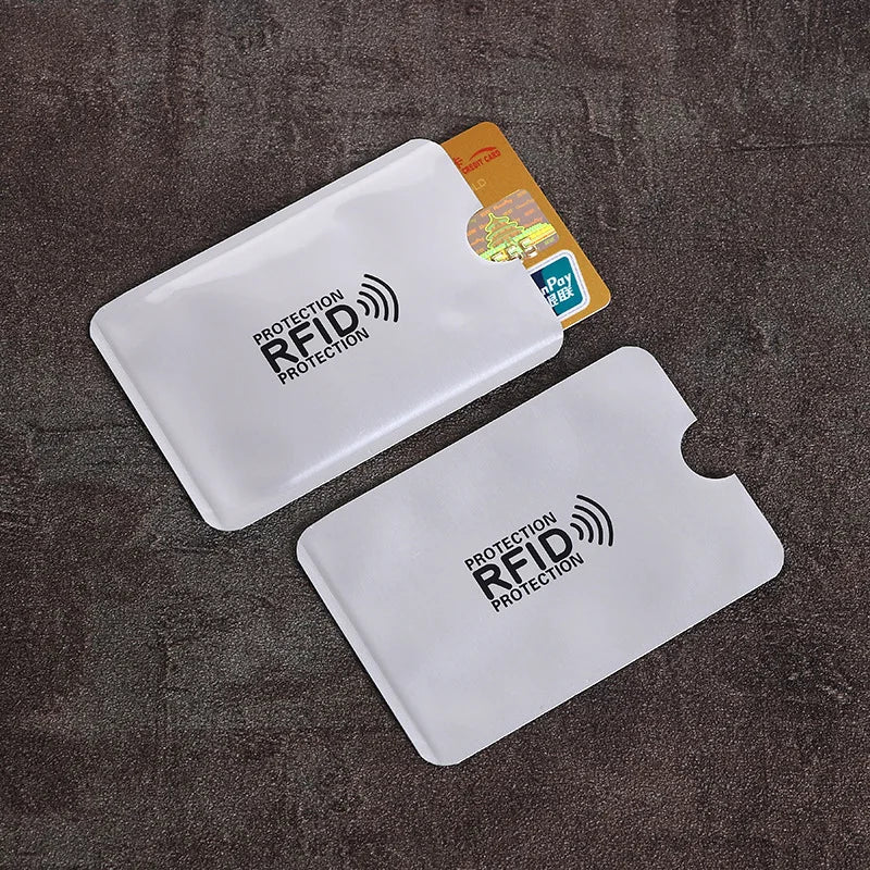 Two white, flat, metallic RFID-blocking card sleeves, one holding a credit card, on a dark textured background.