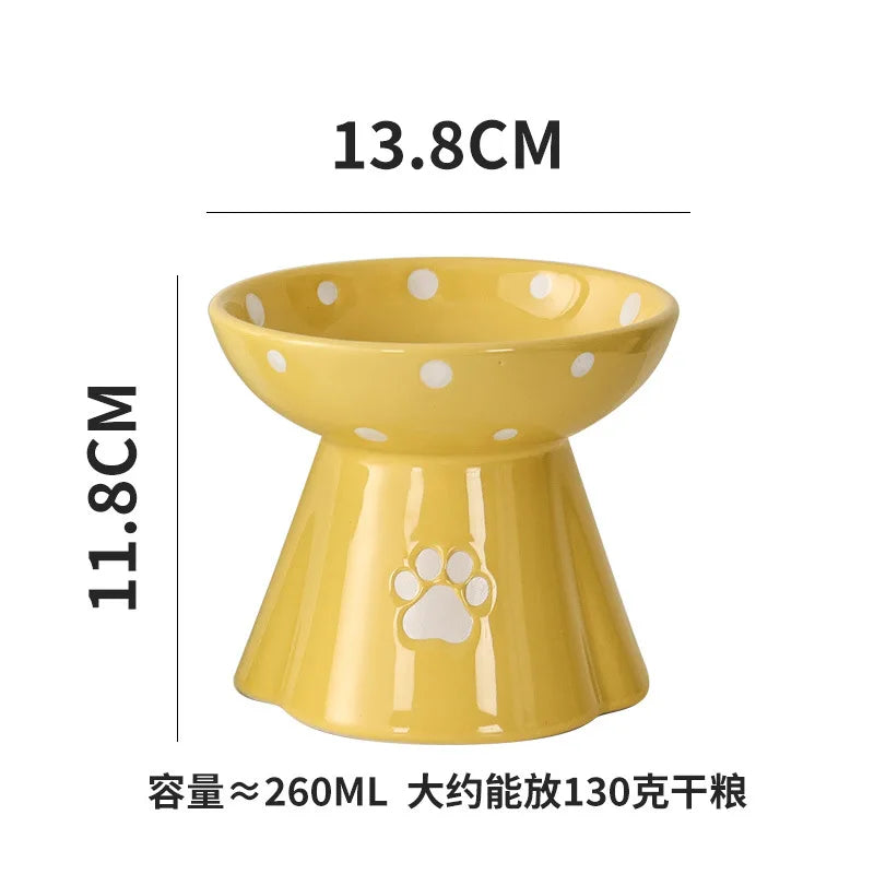 Yellow elevated ceramic cat bowl with white polka dots and a paw print design, measuring 13.8cm wide by 11.8cm high.