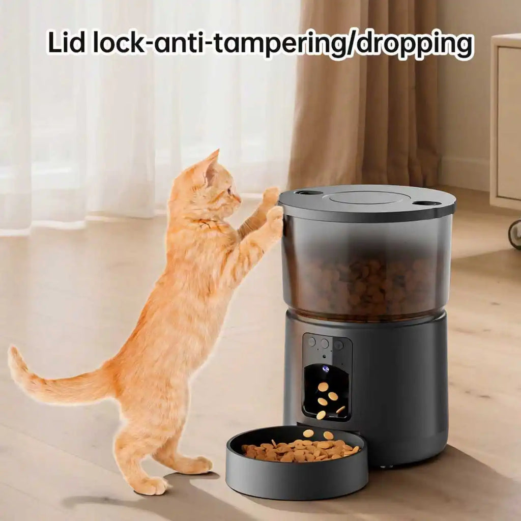Ginger cat reaching for a sleek, dark grey automatic pet feeder with a camera, food hopper and sturdy bowl.