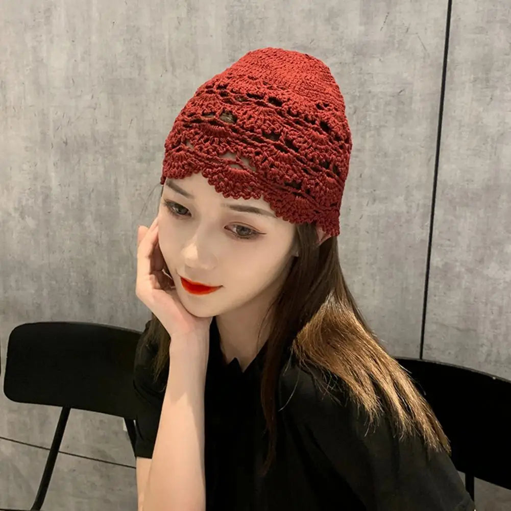 A woman wearing a dark red, hollow crochet lace beanie with a decorative scalloped edge design.
