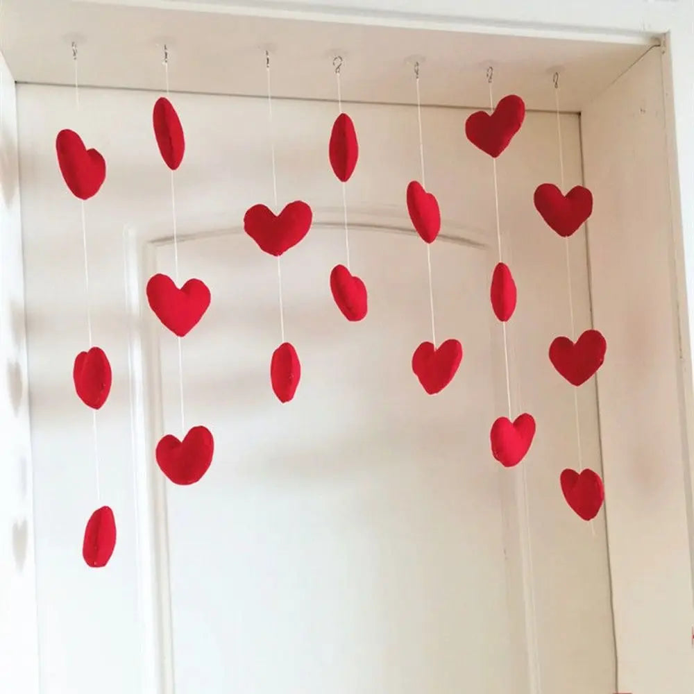 Hanging decoration featuring multiple red fabric hearts suspended on thin white strings against a white door.