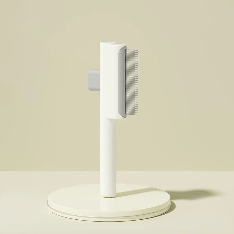 White self-cleaning pet grooming brush with fine metal bristles, standing upright on a matching round base.