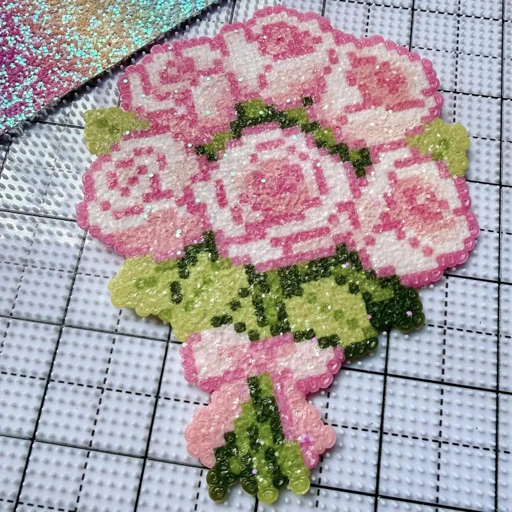 Sparkly pink rose bouquet craft patch with green leaves on a white grid craft mat.
