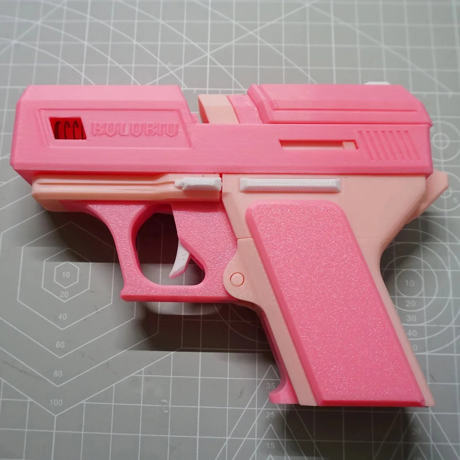 Pink plastic pistol-style AirPods case on a cutting mat. Novelty design with textured and smooth finishes.