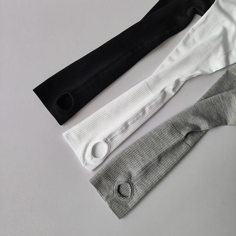 Three long-sleeved athletic tops in black, white, and grey with ribbed texture and integrated thumbhole cuffs.