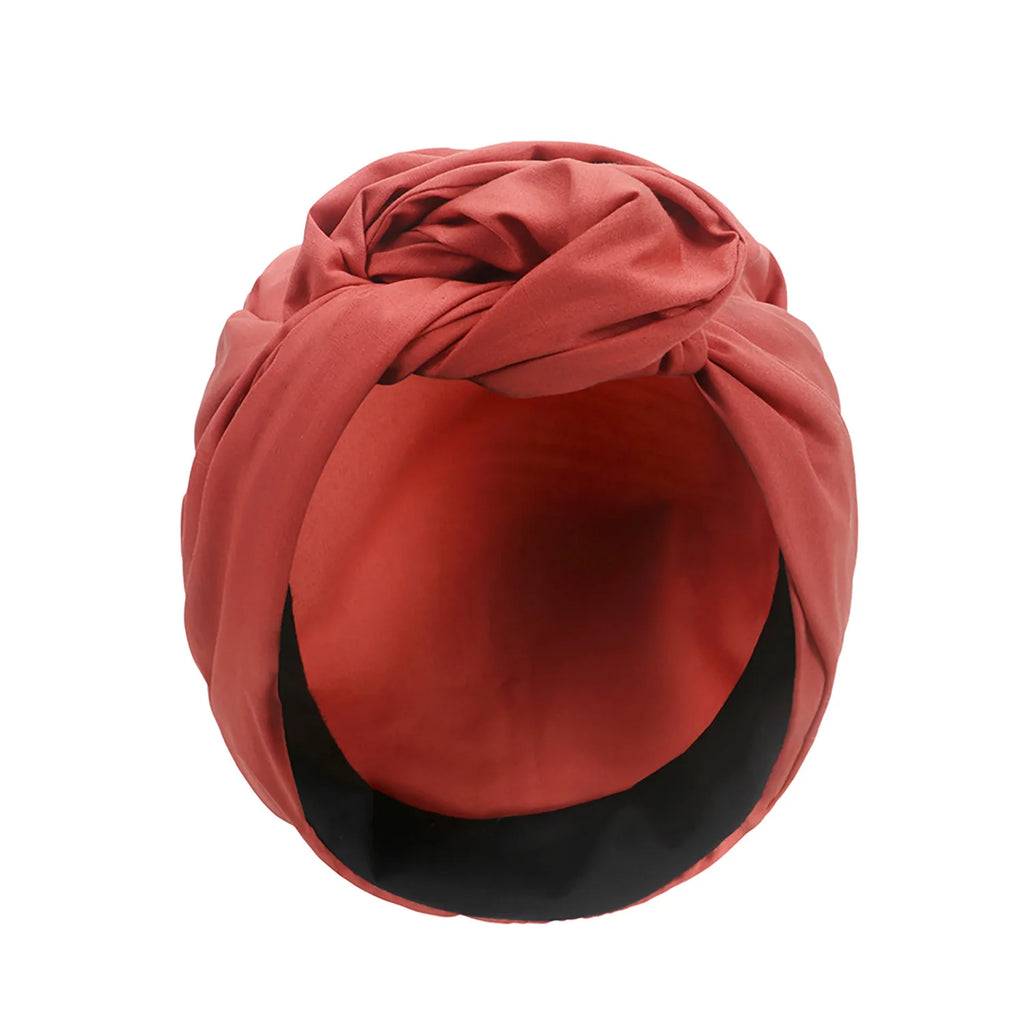 A vintage-style, terracotta-red turban hat featuring a decorative front knot and a smooth black inner lining.