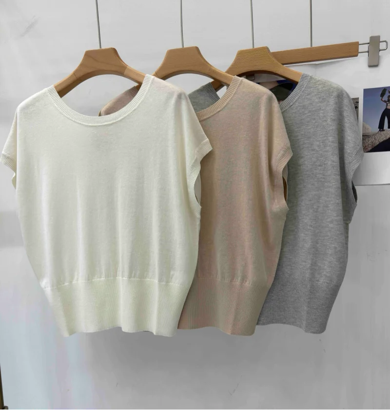 Three lightweight, short-sleeved knitted sweater vests in white, beige, and grey with a ribbed hem on wooden hangers.