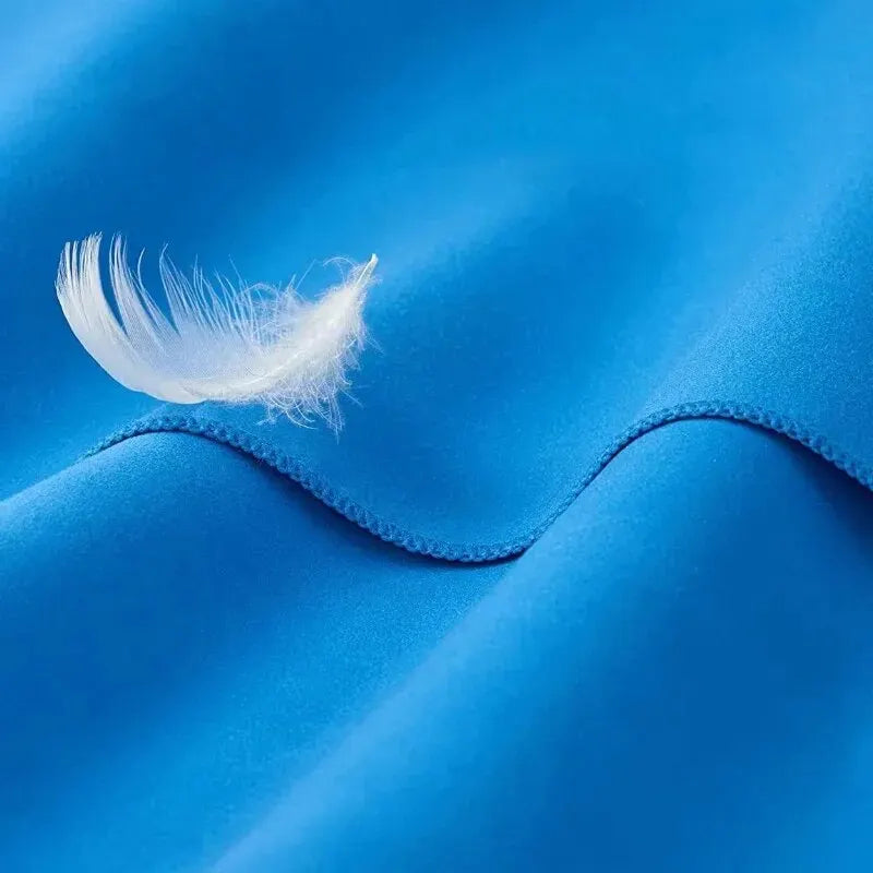 A single white feather resting on soft, vibrant blue fabric with a stitched hem.