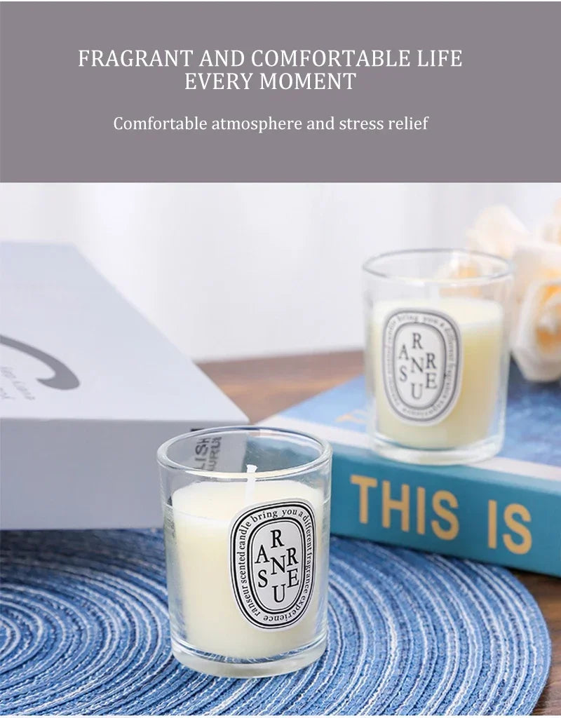 Two small, cream-coloured scented candles in glass jars with minimalist oval labels, set on a blue textured mat.