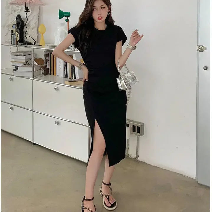 Woman wearing a black short-sleeved midi dress with a side split, paired with a metallic silver handbag.