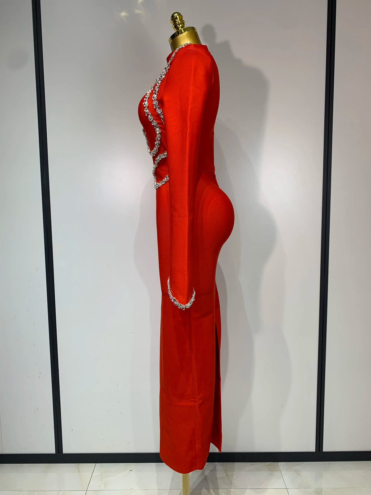 Red long-sleeve bodycon maxi dress featuring sparkling rhinestone trim and a side slit, shown on a mannequin.