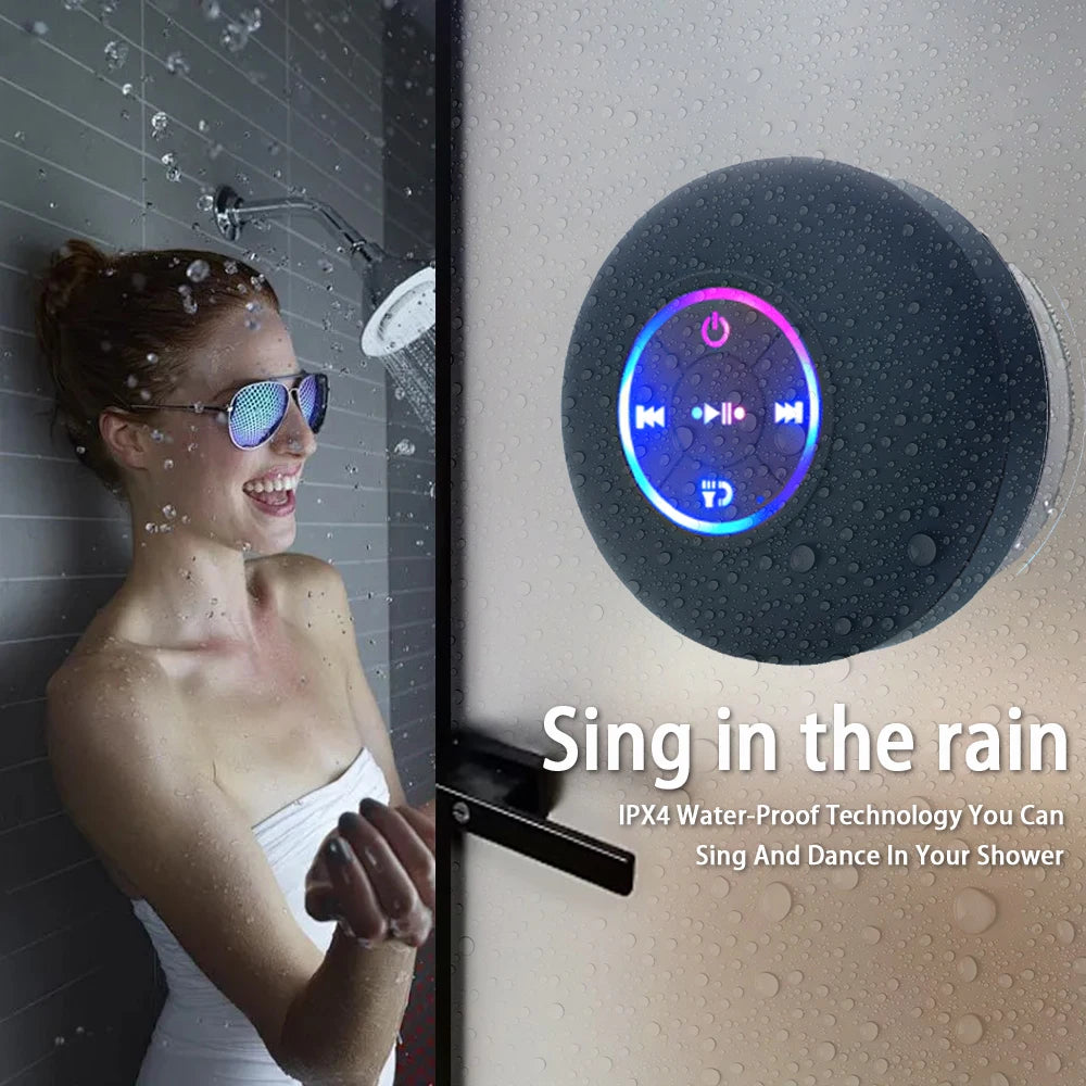 Black circular waterproof Bluetooth shower speaker with glowing multicolour LED buttons, mounted on a wet wall.