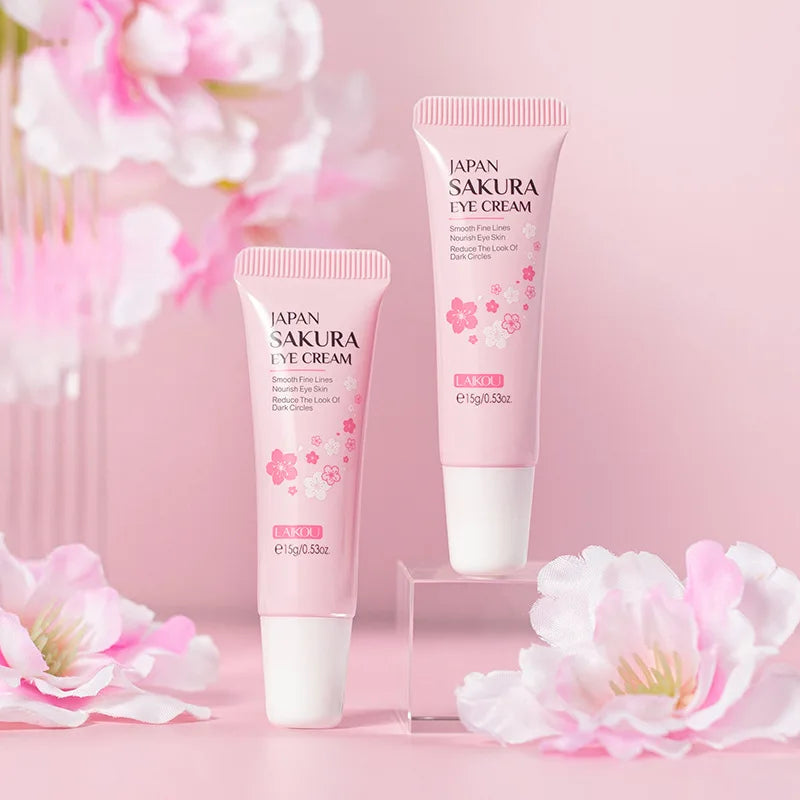 Two pink tubes of sakura eye cream on a display stand, decorated with cherry blossom flowers on a soft pink background.