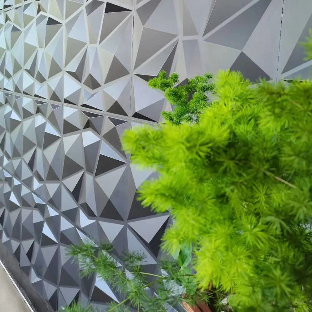 Grey 3D geometric wall tiles with a modern diamond pattern, partially obscured by a bright green decorative plant.