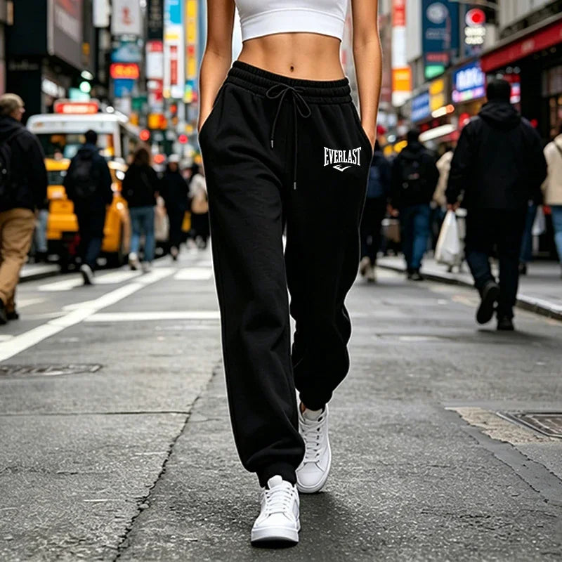 Woman wearing comfortable black joggers with an elasticated drawstring waist and cuffed hems, paired with white trainers.