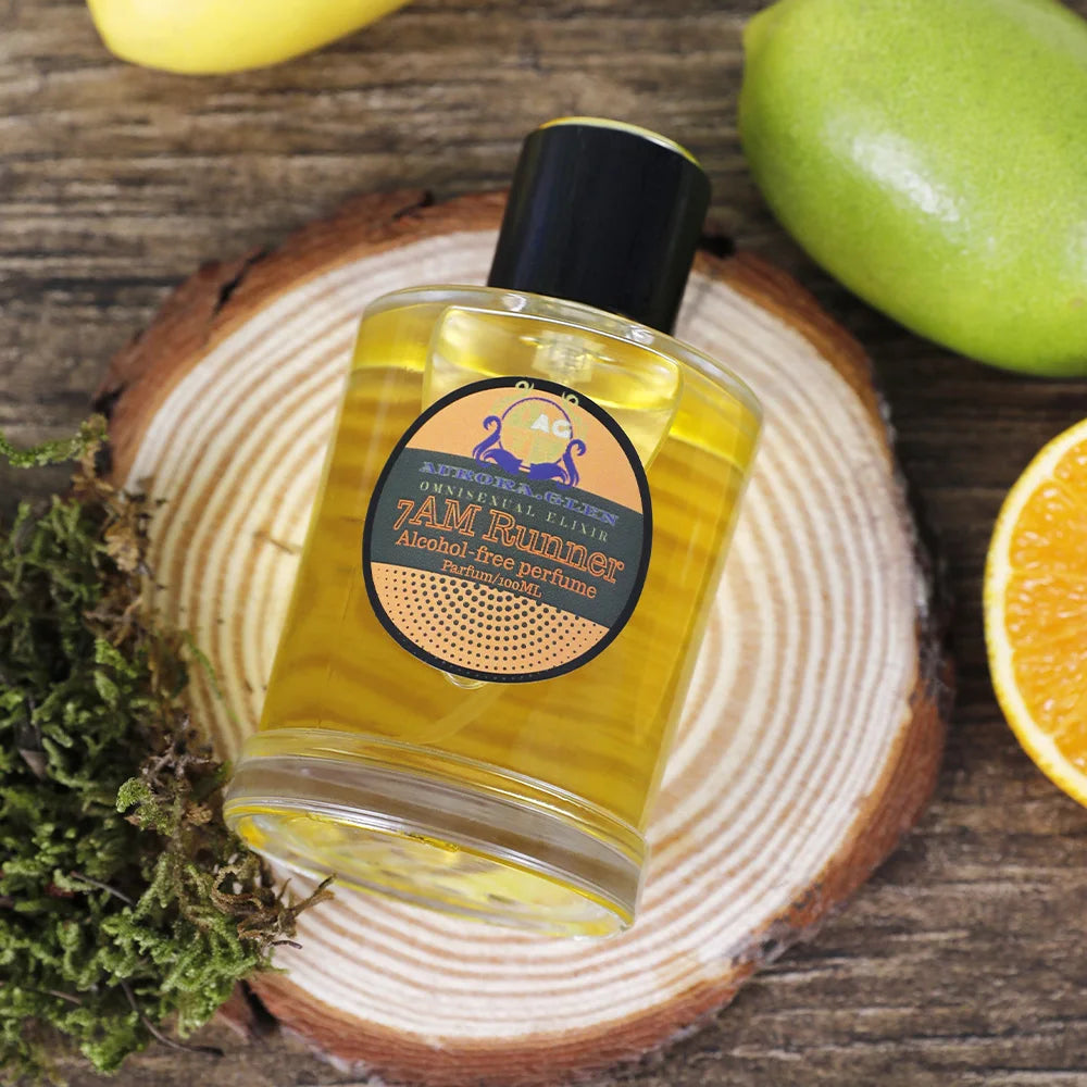 Glass bottle of yellow alcohol-free perfume on a wood slice, surrounded by fresh citrus fruits and green moss.