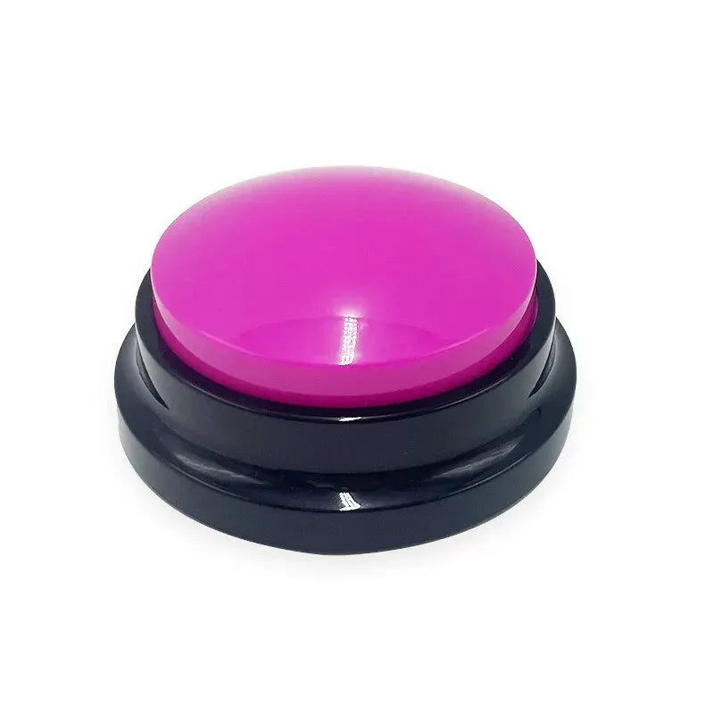 A round, interactive dog training button with a bright pink top and black circular base on a white background.