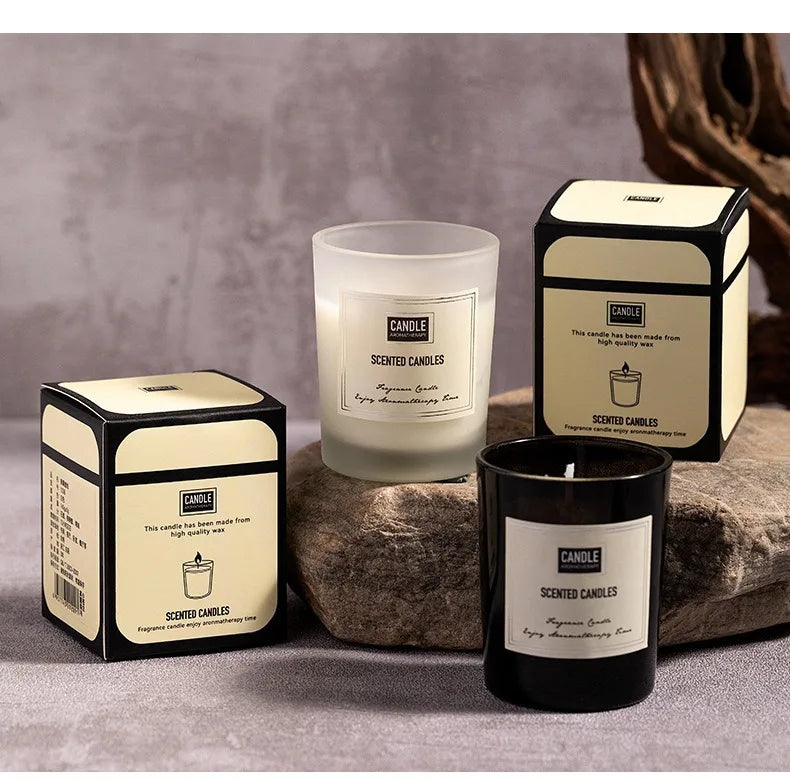 Two scented candles in white frosted and black glass jars, each with matching cream and black gift boxes.