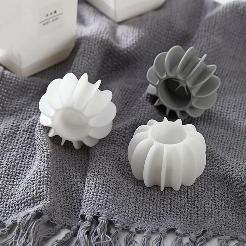 Two white and one grey silicone, pumpkin-shaped ring holders sitting on a grey textured fabric surface.