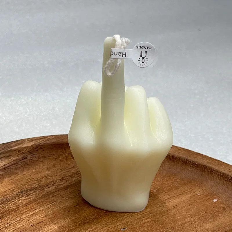 Off-white candle shaped like a hand making a middle finger gesture, sitting on a wooden dish.
