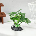 Artificial green variegated plant with sturdy stems rooted on a textured black stone base for aquarium use.
