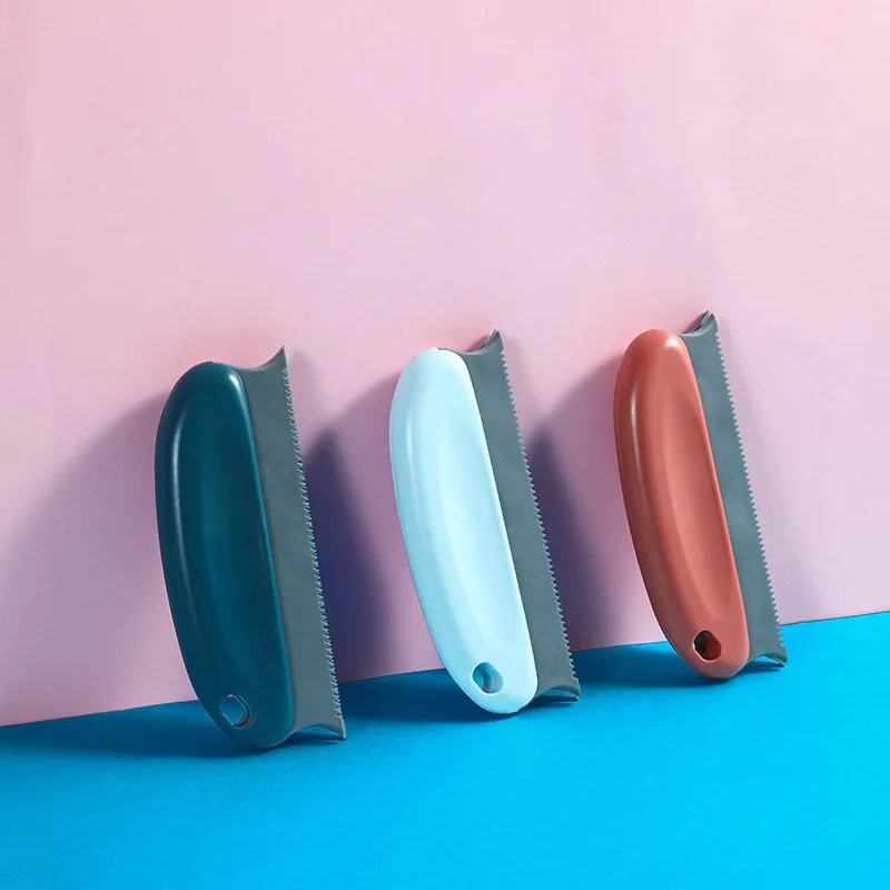 Three handheld lint removers in dark teal, light blue, and coral, each with a grey serrated edge and hanging hole.