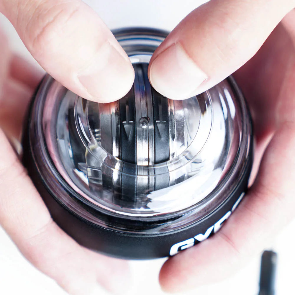 Hands holding a black and clear plastic wrist exercise gyro ball with a visible inner metal rotor.