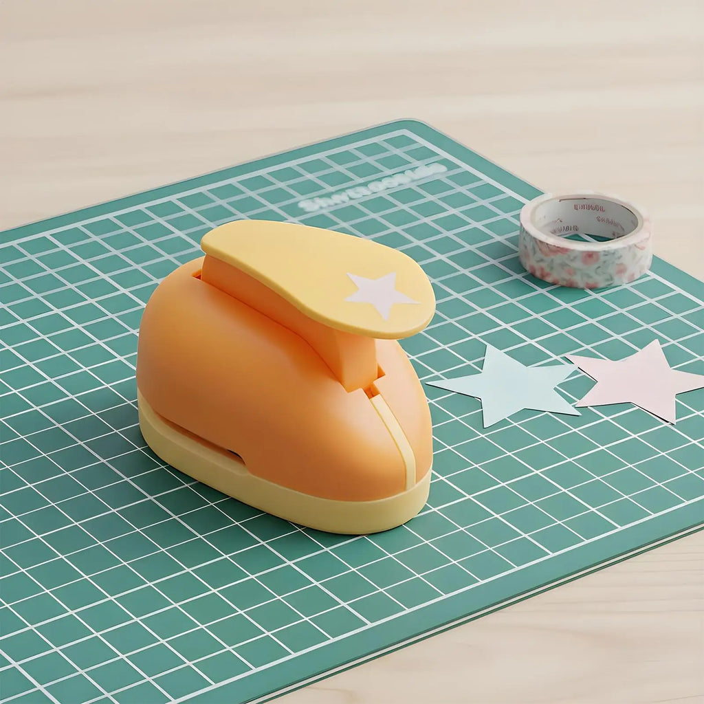 Orange star-shaped paper craft puncher on a green cutting mat with paper stars and a roll of patterned tape.