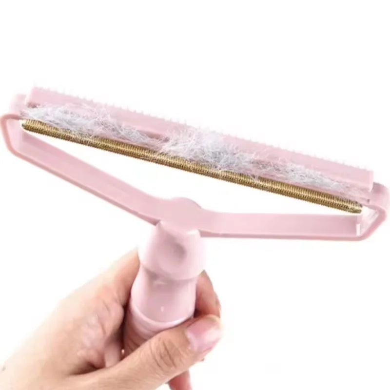 A hand holding a pastel pink fabric lint remover tool with a metallic scraping edge covered in collected fluff.