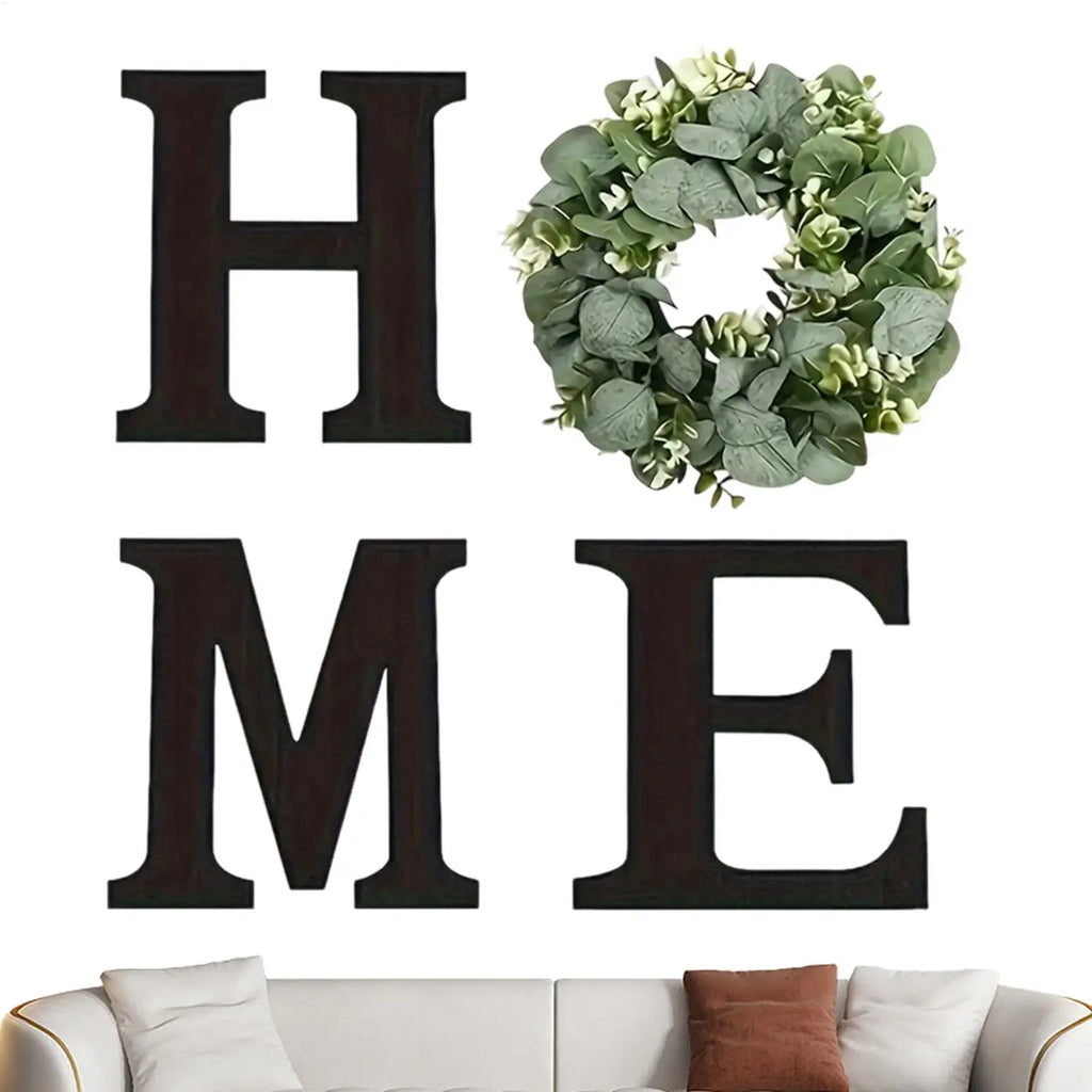 Rustic black wooden letters spelling HOME, featuring an artificial green eucalyptus wreath as the letter O.