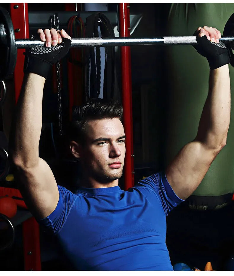 A man in a blue t-shirt lifting a barbell, wearing black gym gloves with a white honeycomb-patterned grip.