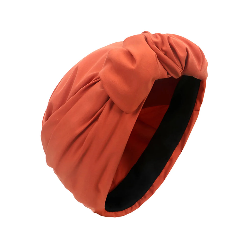 A burnt-orange vintage-style turban hat featuring a gathered knotted front and a black interior lining.