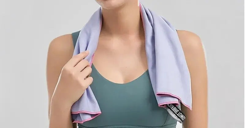 A light purple cooling gym towel with pink stitching draped around a person’s neck wearing a teal sports bra.