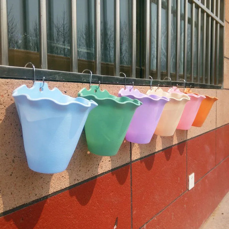 A row of colorful, ruffled-edge plastic planters hanging from a metal window grate against a brick wall.