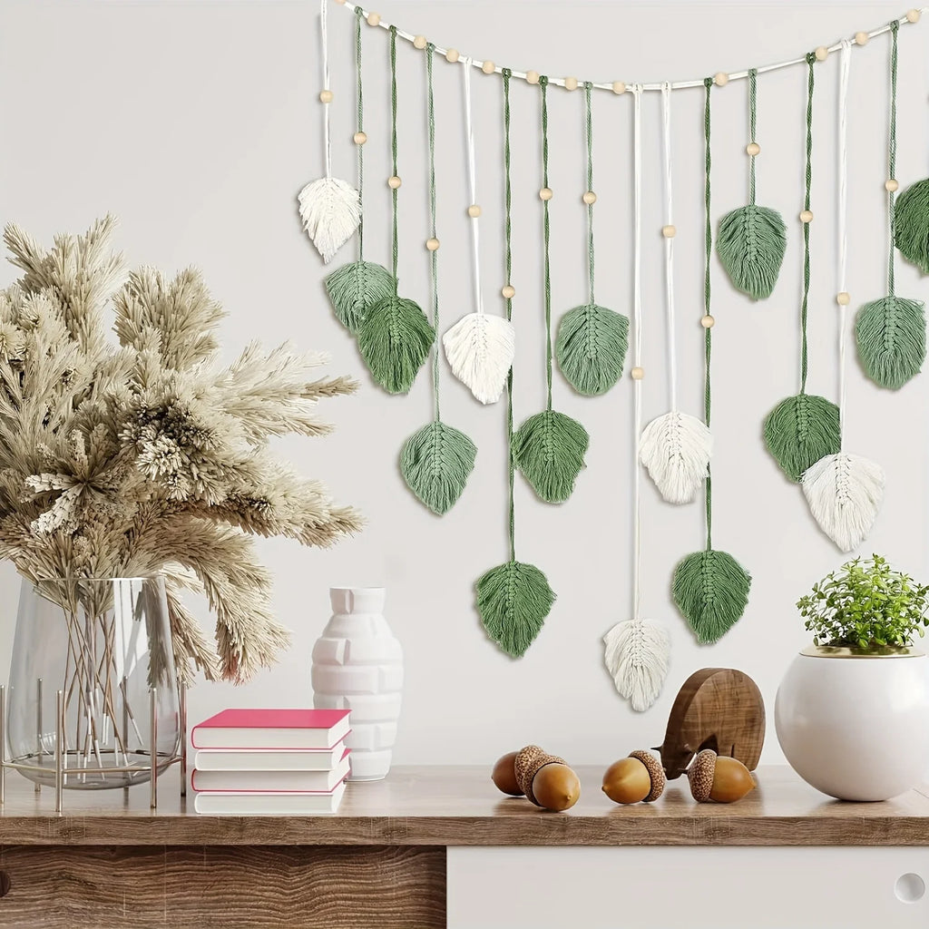 Boho macrame wall hanging featuring sage green and cream leaf motifs on strings accented with wooden beads.