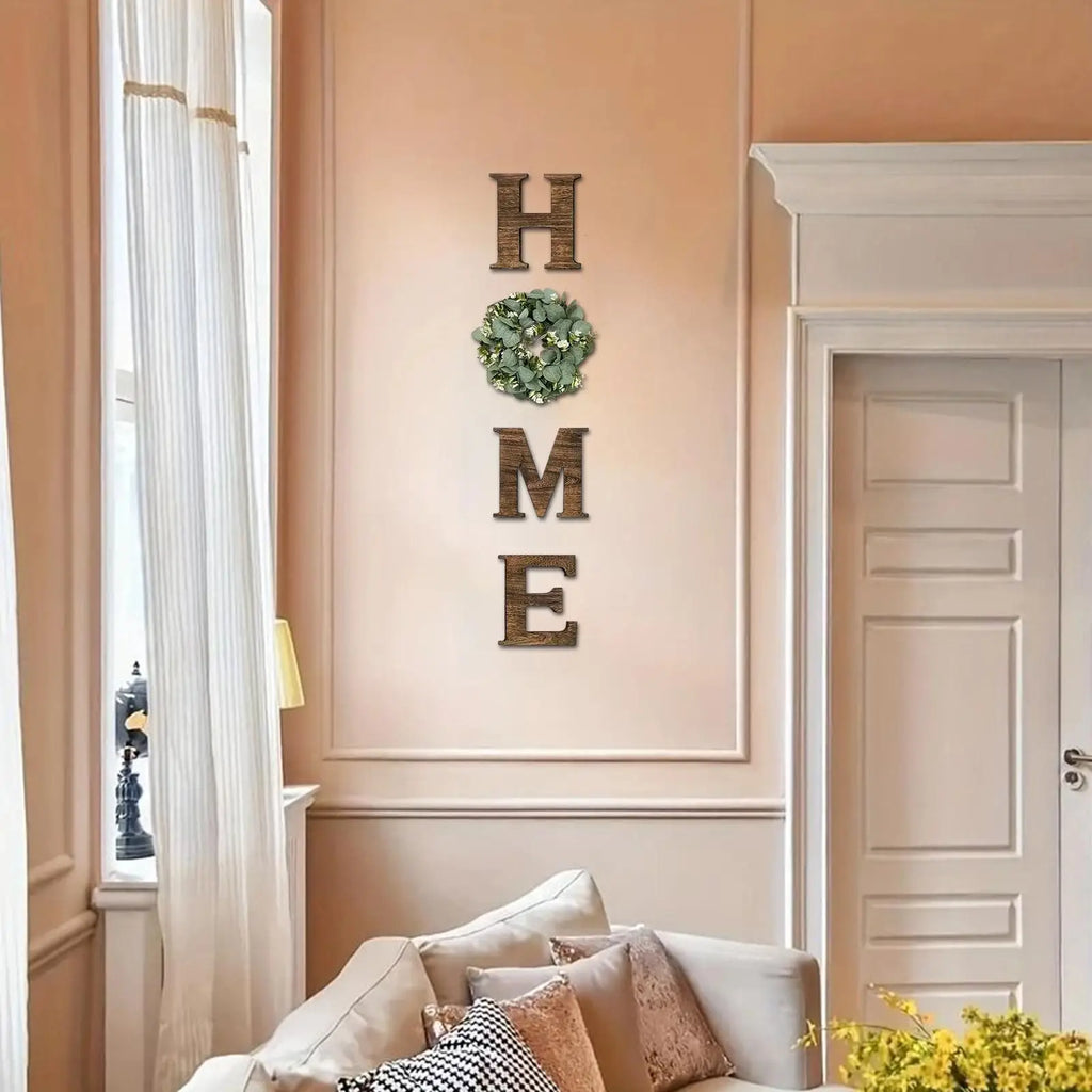 Rustic wooden 'HOME' wall letters with a decorative green artificial eucalyptus wreath replacing the letter 'O'.