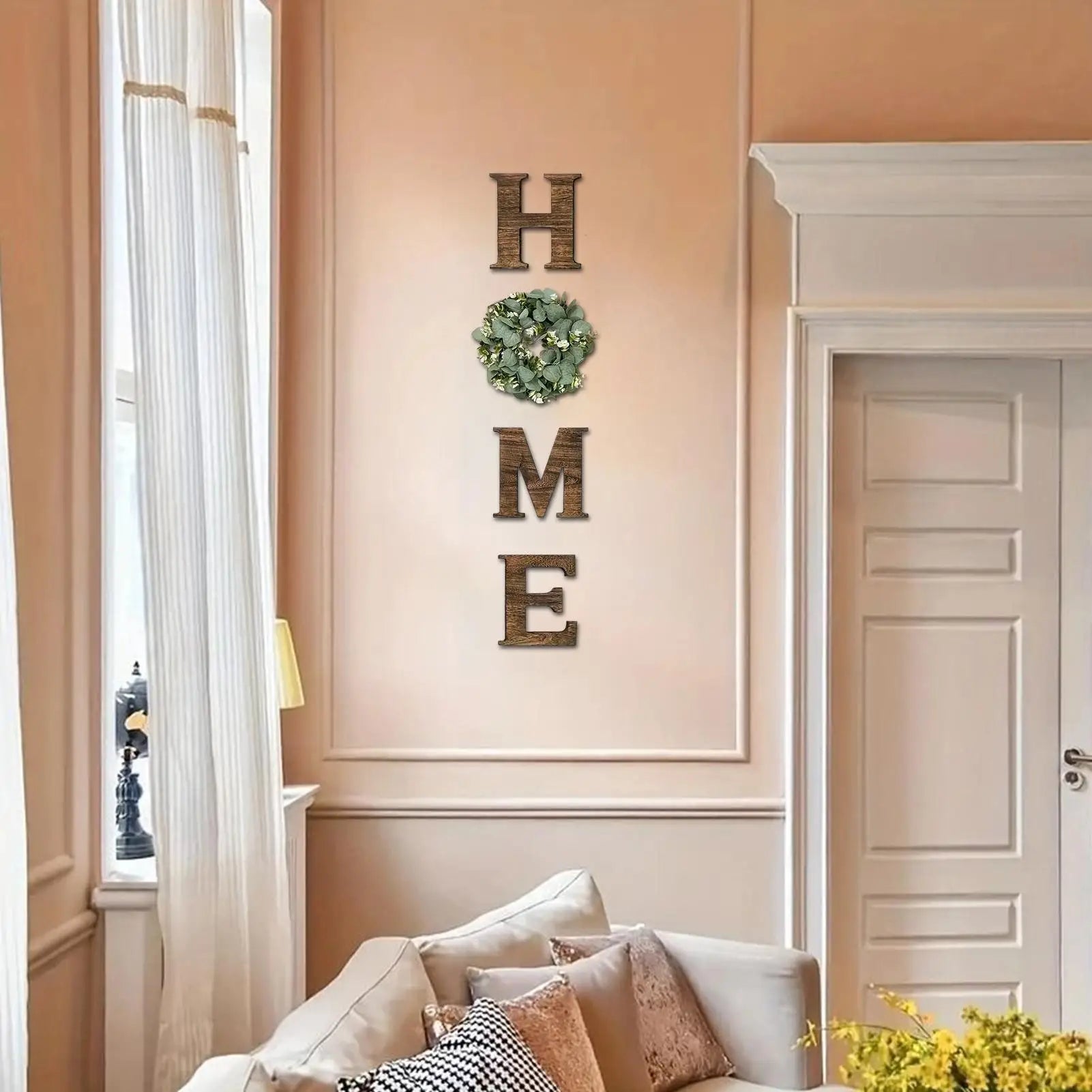 Rustic wooden 'HOME' wall letters with a decorative green artificial eucalyptus wreath replacing the letter 'O'.